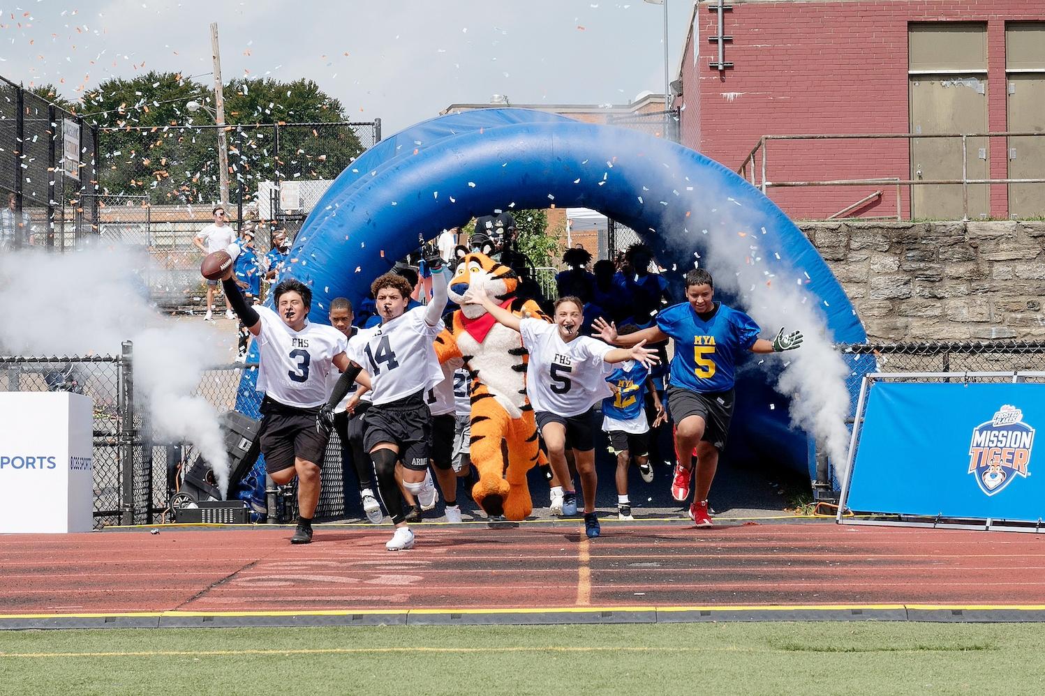 Students run onto a football field with Tony the Tiger as part of Mission Tiger. 